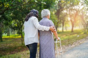dark-haired woman helping elderly woman with walker outside
